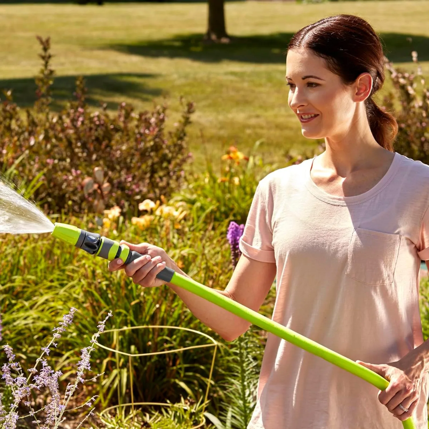 A woman watering a perennial bed with the chartreuse Flexzilla hose and nozzle at golden hour