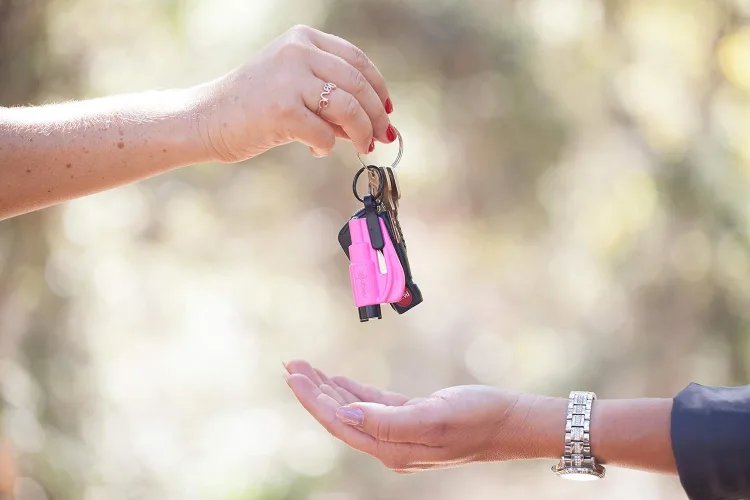 A resqme tool on a keyring being handed from one hand to another — the size of a car key.